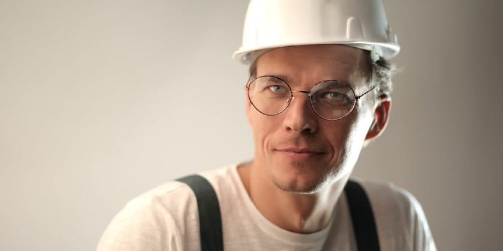 Content male builder in workwear and hardhat smiling on gray background in studio and looking at camera